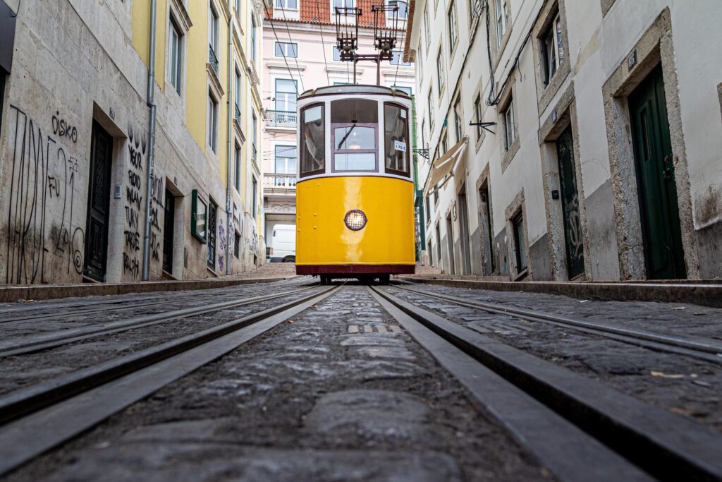 Yellow tram going down narrow alley surrounded by old buildings — Portugal